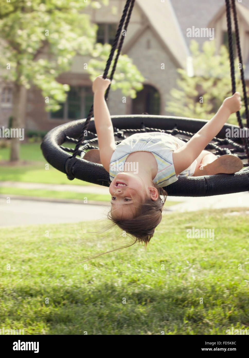 Young girl hanging upside down from her swing and smiling. Stock Photo