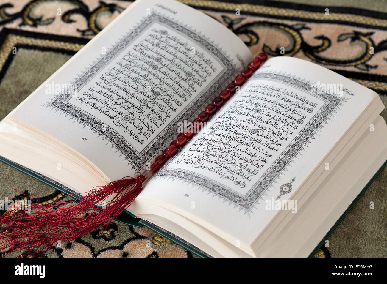 Open Koran book and the prayer beads on a carpet Stock Photo