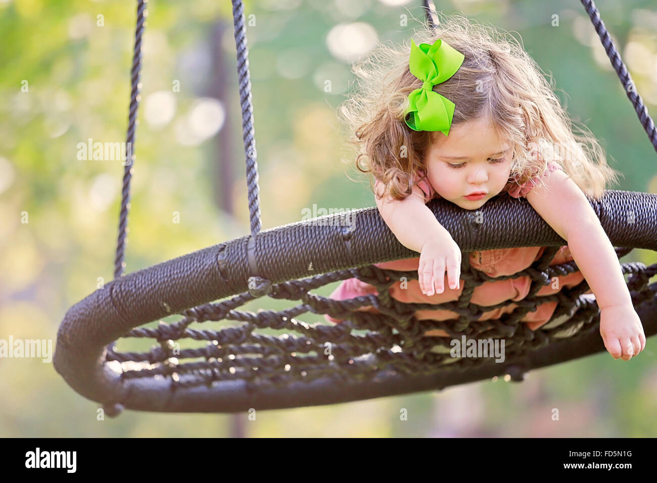 Toddler girl laying on her stomach on a swing as if pretending to fly. Stock Photo