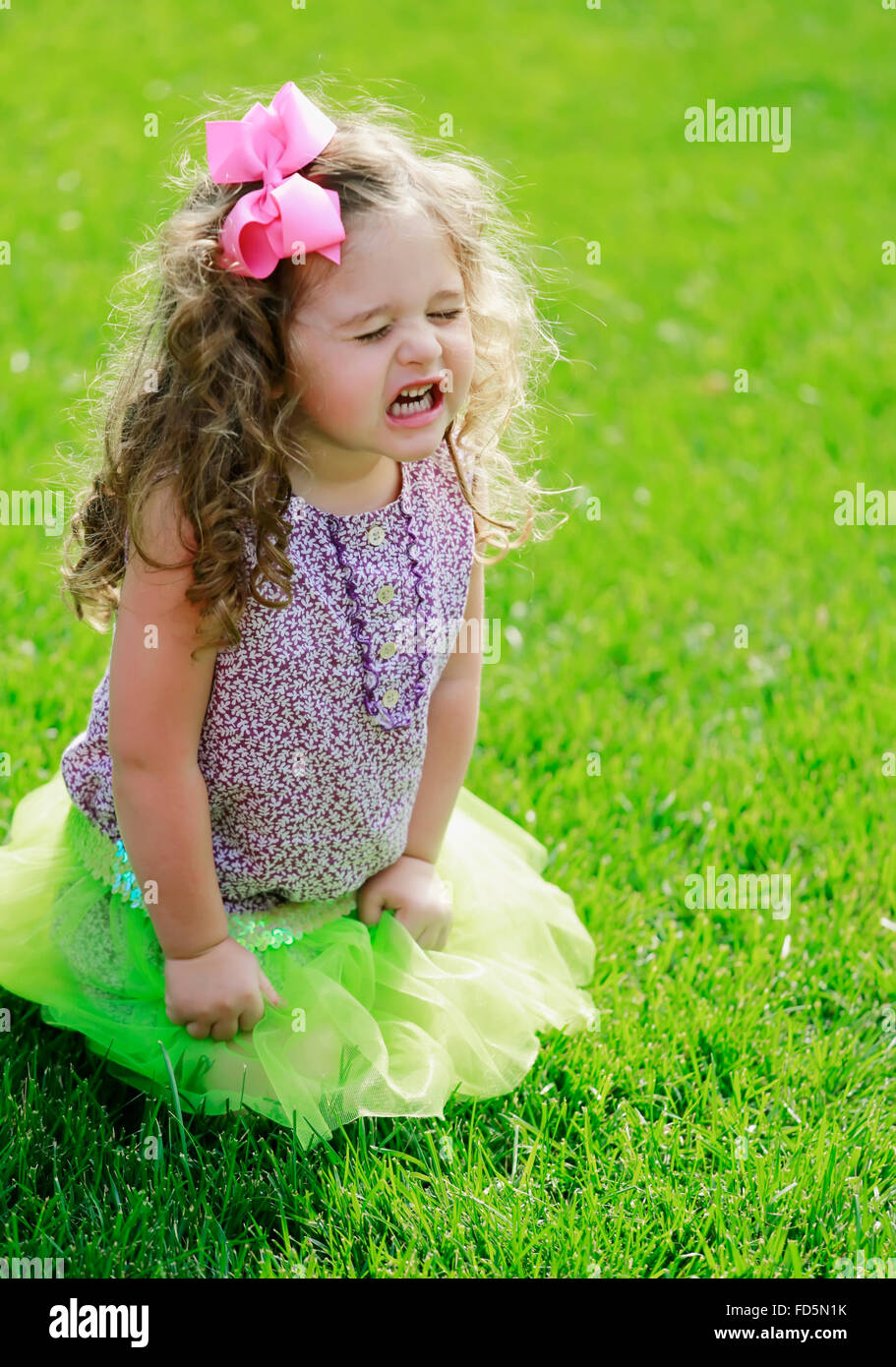 Toddler girl kneeling in the grass with a very frustrated expression on her face. Stock Photo