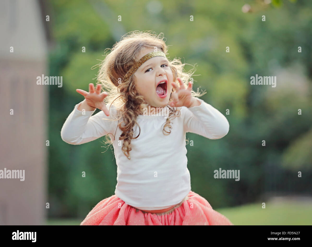 Toddler girl pretending to roar like a lion while playing outside. Stock Photo
