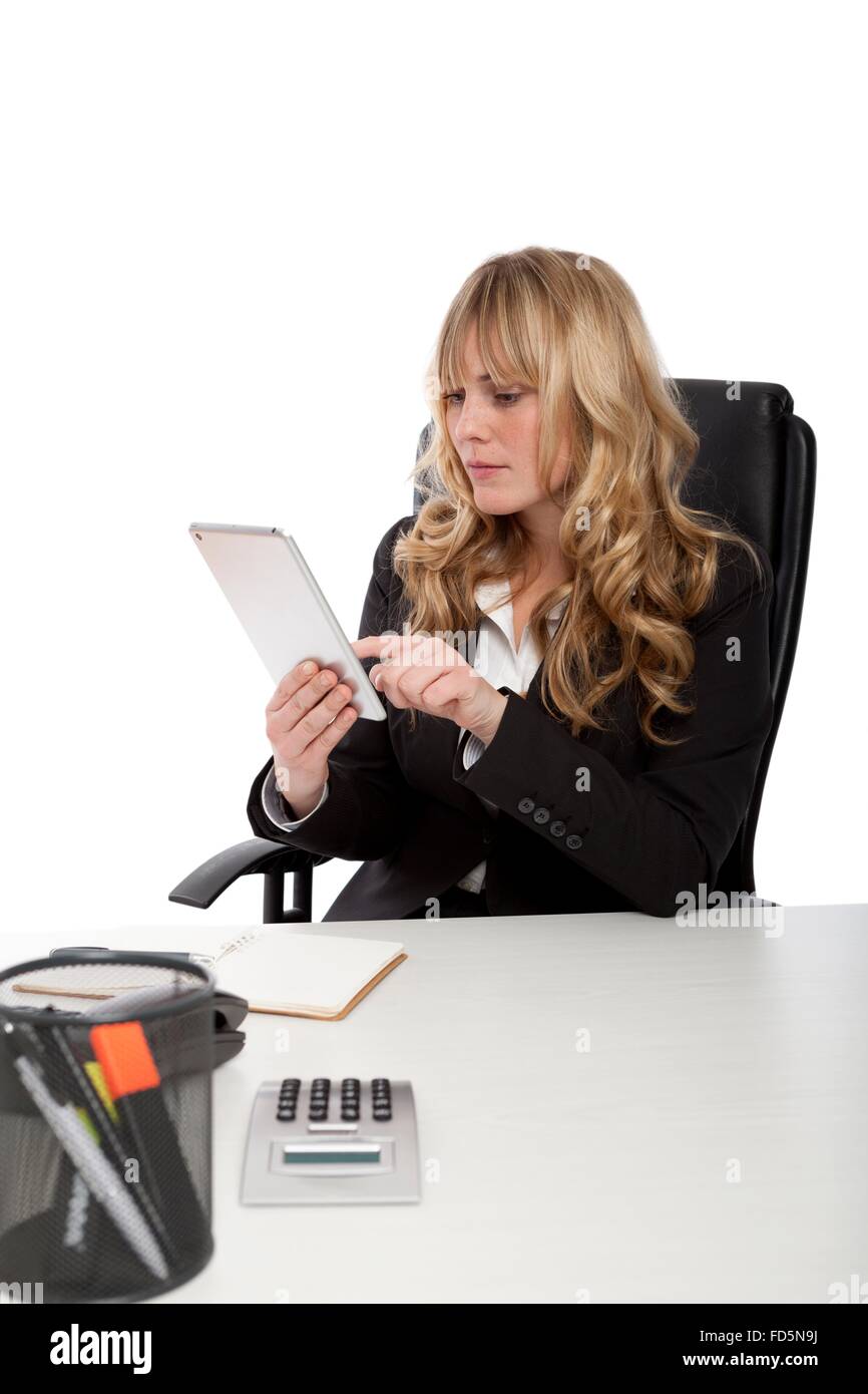 Attractive young office worker using a tablet computer as she sits at her desk conducting her business, on white Stock Photo