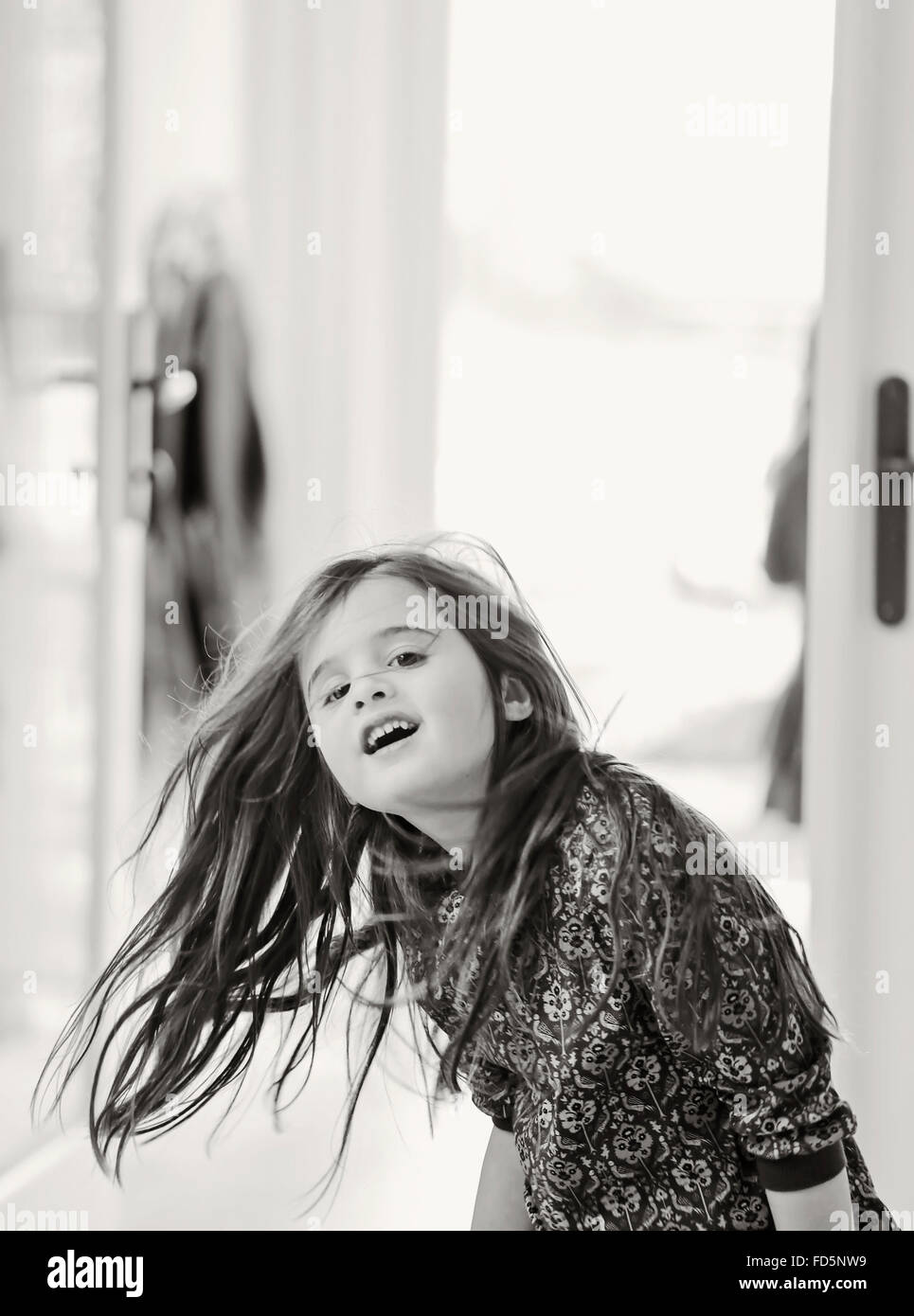 Black and white image of a young girl dancing and playing, swinging her long, brown hair and smiling. Stock Photo