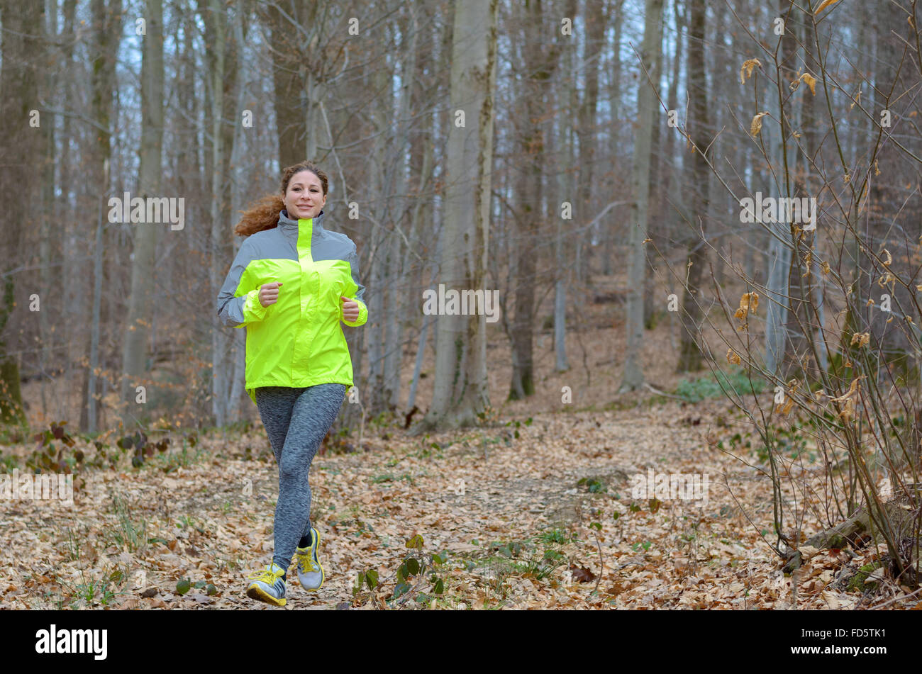 Young woman jogging through winter woodland wearing a high visibility top for safety as she enjoys her daily workout in a health Stock Photo