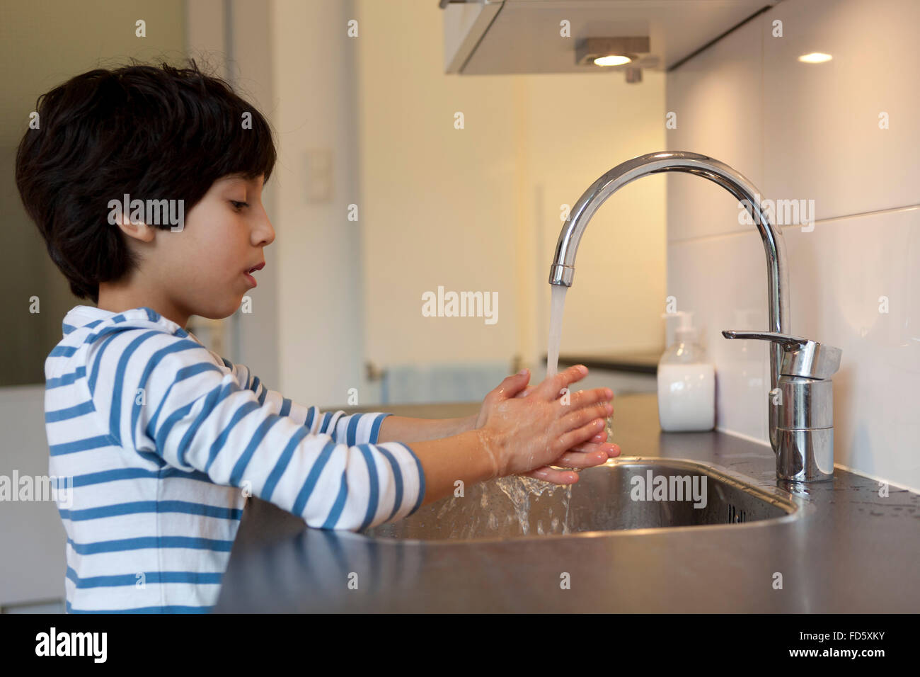 Eight year old boy washing hands in the kitchen Stock Photo