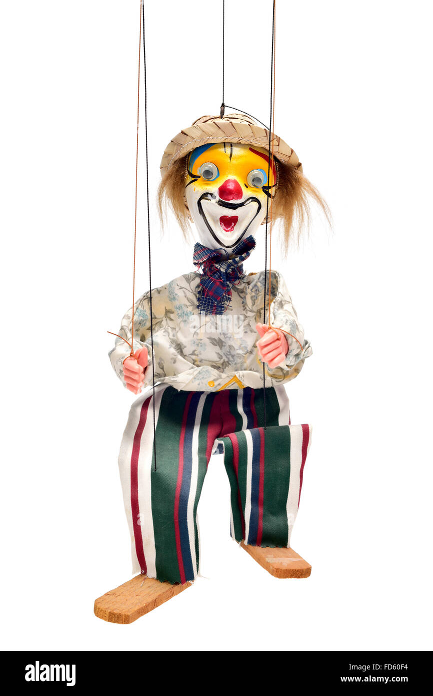 an old marionette with its face painted like a clown being manipulated against a white background Stock Photo