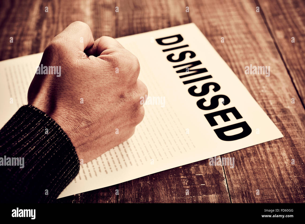 closeup of the fist of a young caucasian man on a document with the text dismissed, placed on a rustic wooden table Stock Photo