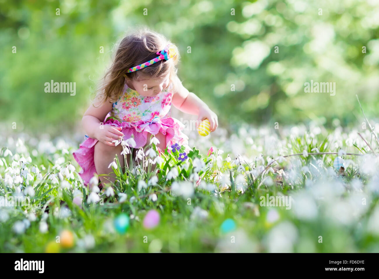 Little girl having fun on Easter egg hunt. Kids in blooming spring garden with crocus and snowdrop flowers. Stock Photo