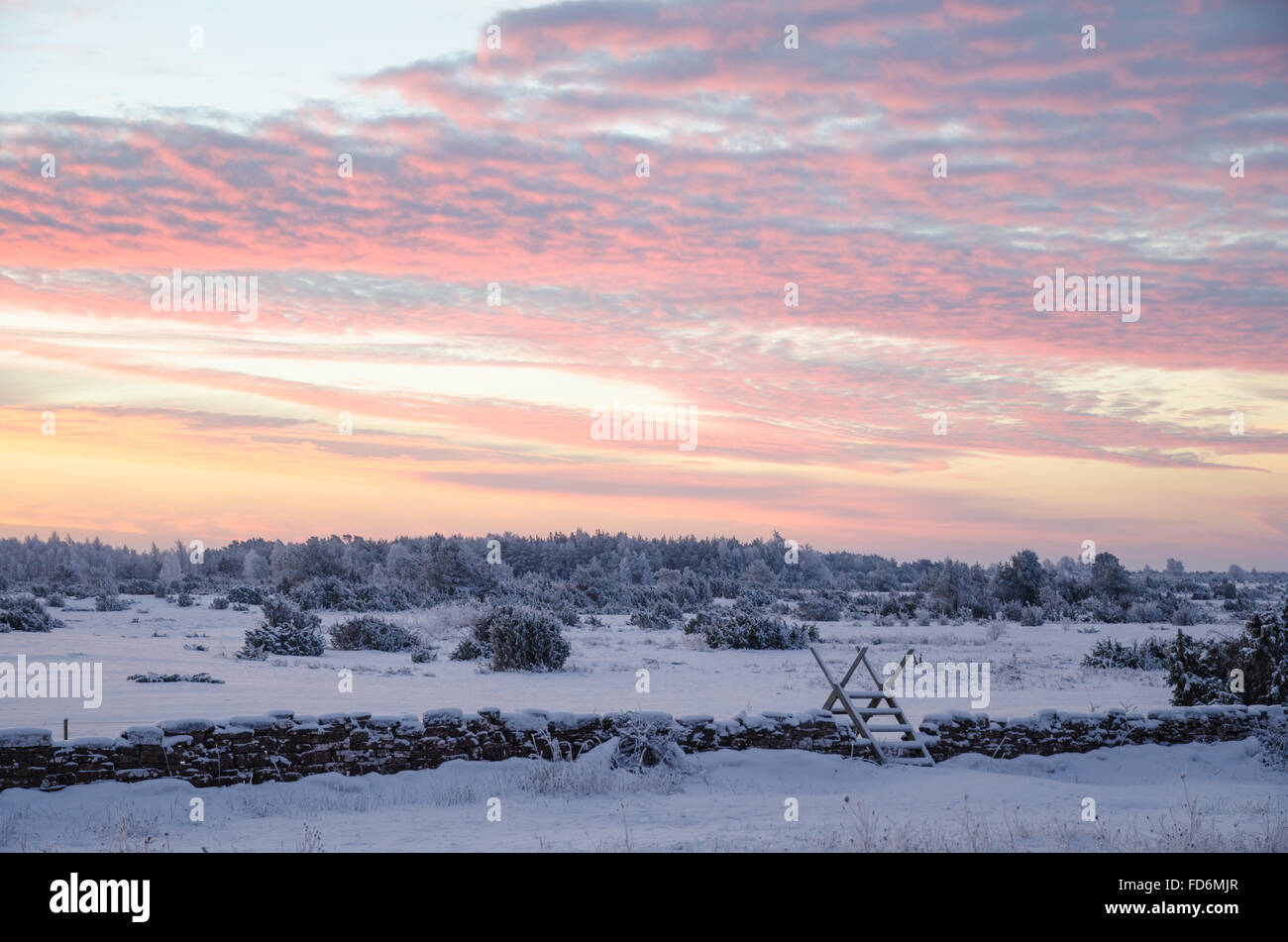 Stile at a stone wall by sunrise in a winter landscape Stock Photo