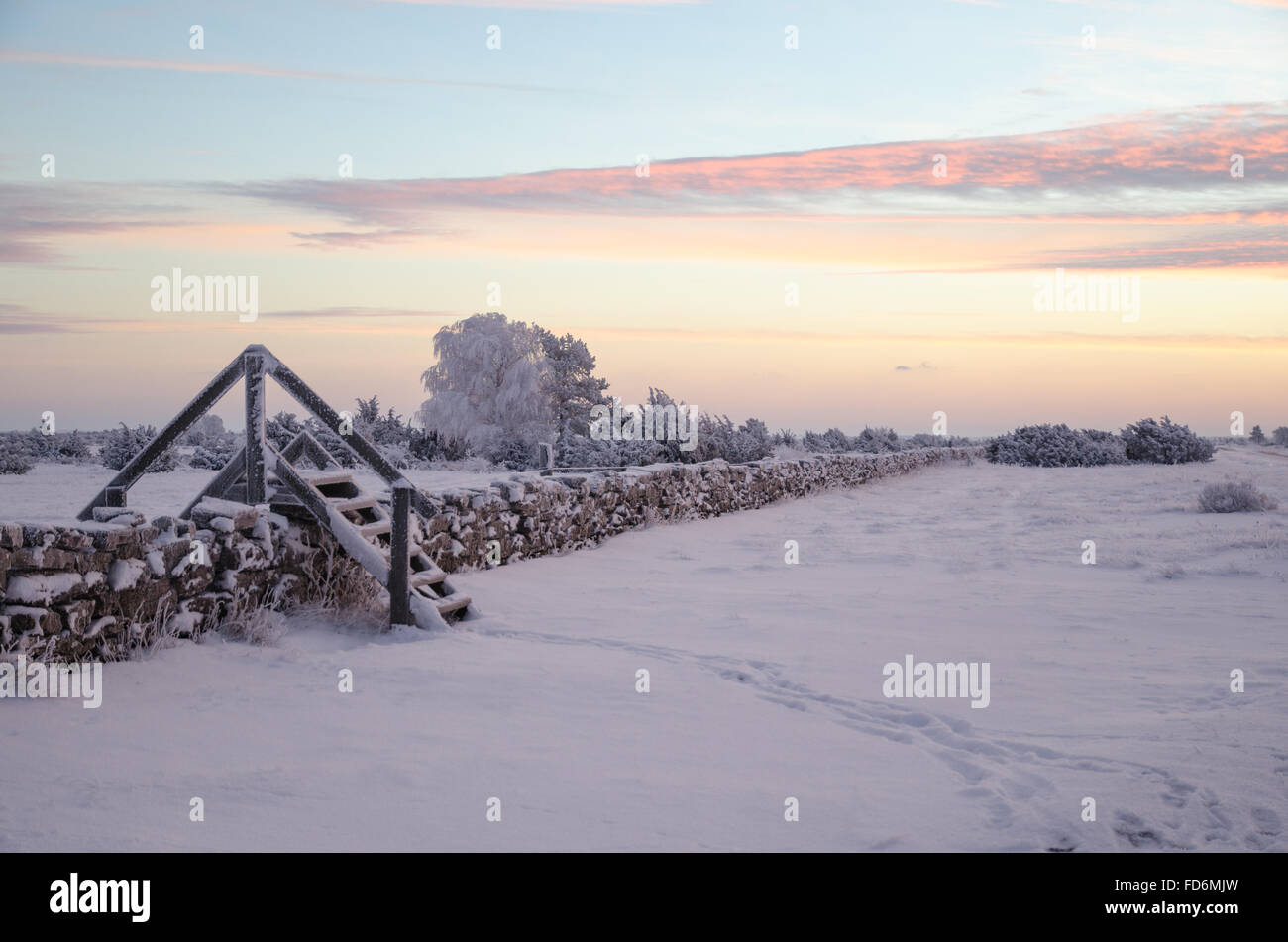 Dawn at a winter landscape with a stile by stone wall Stock Photo