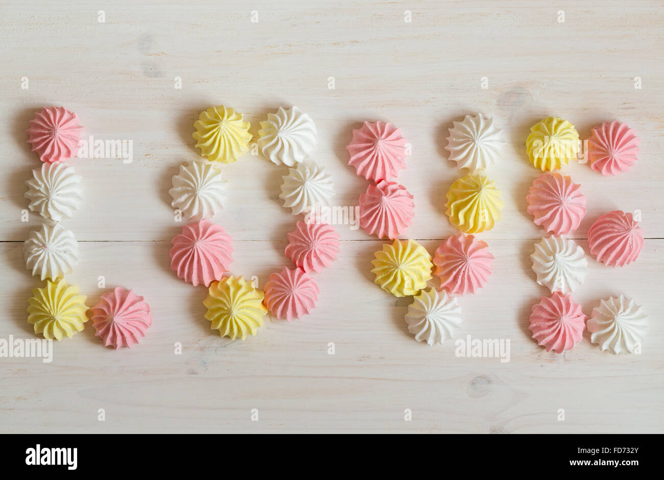 Inscription love meringue made of pastel colors on a white wooden background. Image of Valentines day Stock Photo