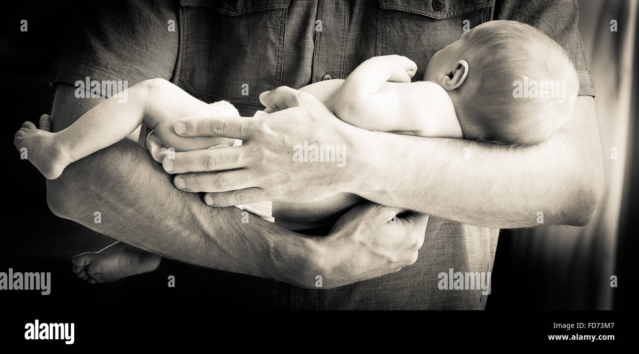 Cute newborn baby boy being held in his father's arms Stock Photo