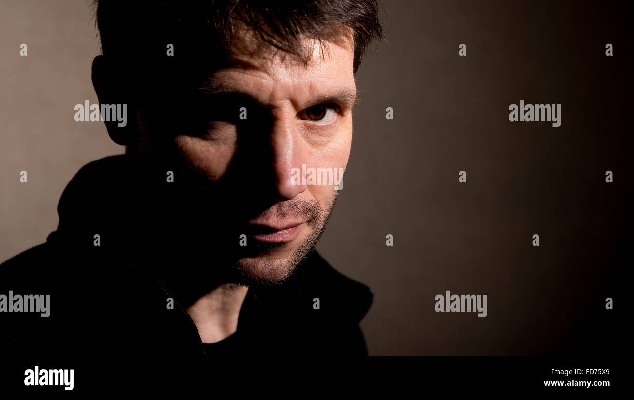 Head and shoulders portrait, of a man with half his face in shadow, and staring at the viewer with a sinister look. Stock Photo