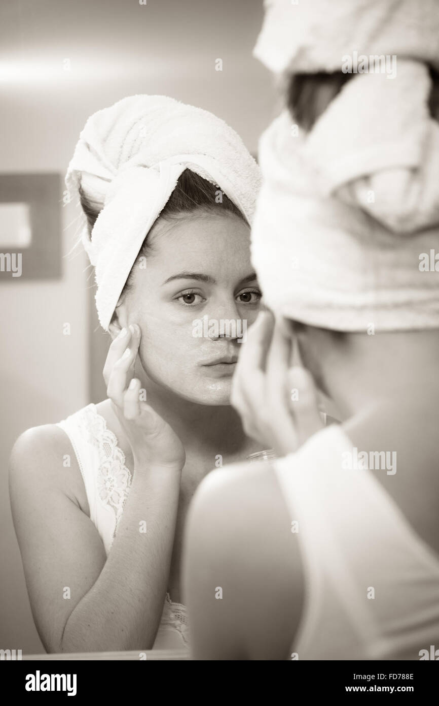 Woman applying mask moisturizing skin cream on face looking in bathroom