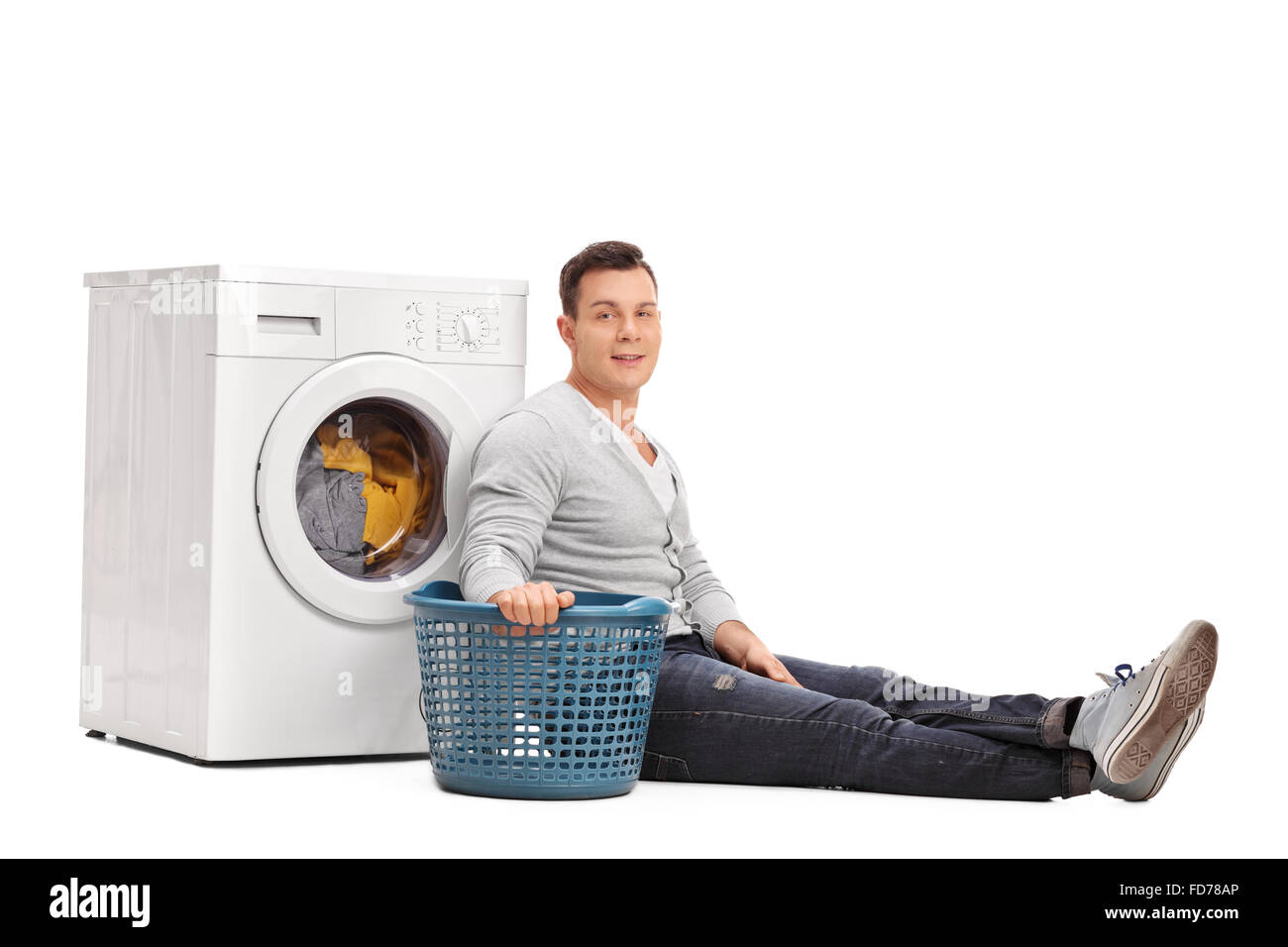 Studio shot of a young man sitting by a washing machine and doing laundry isolated on white background Stock Photo