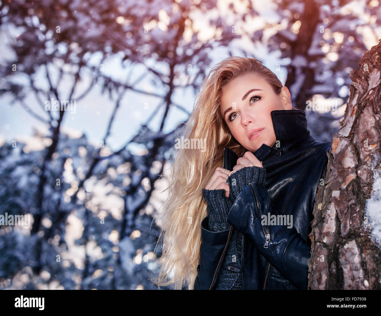Portrait of beautiful blond woman standing near tree in the winter park, fashionable clothing, gorgeous model posing outdoors Stock Photo