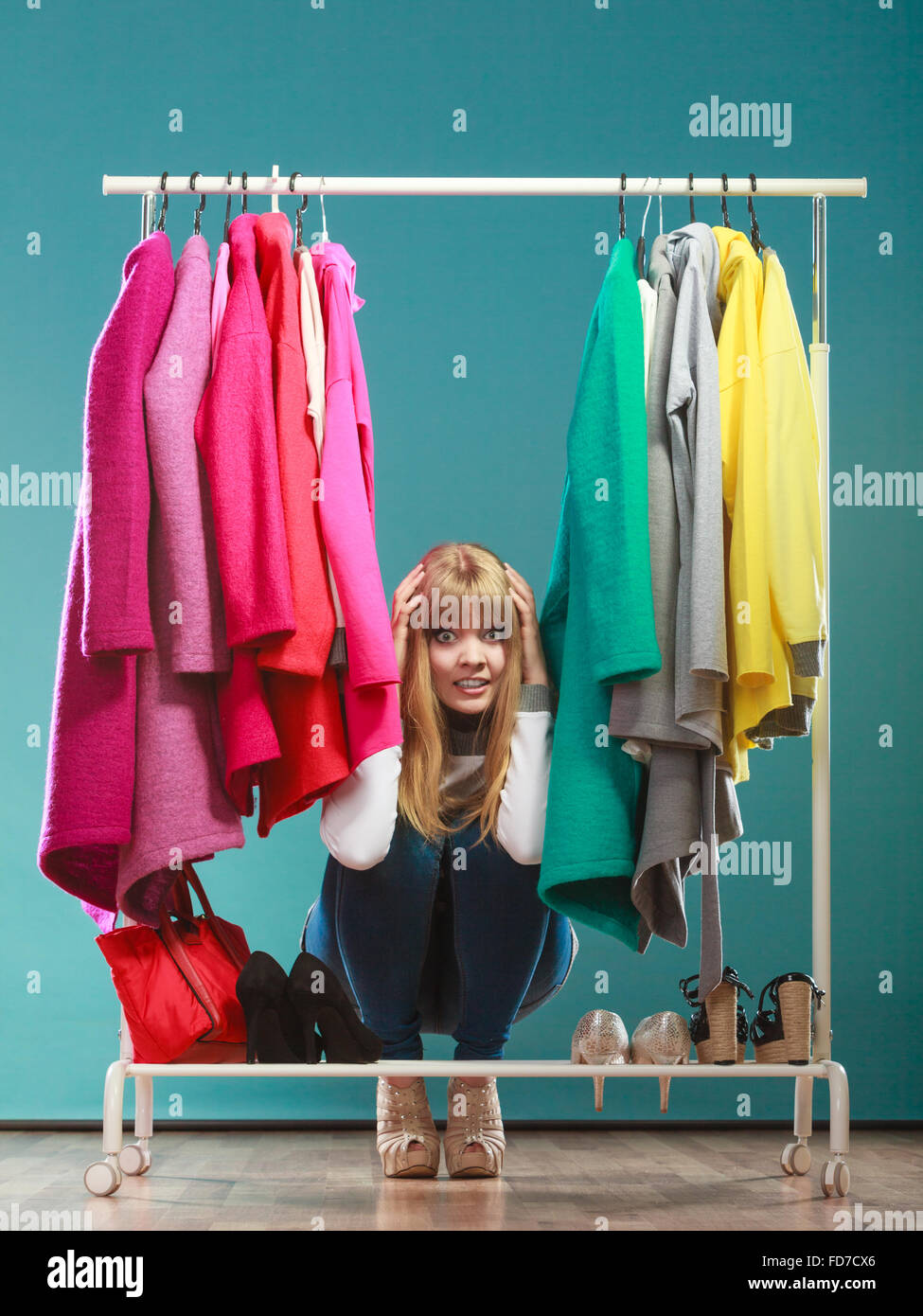 Scared pretty woman hiding among clothes in wardrobe. Attractive young