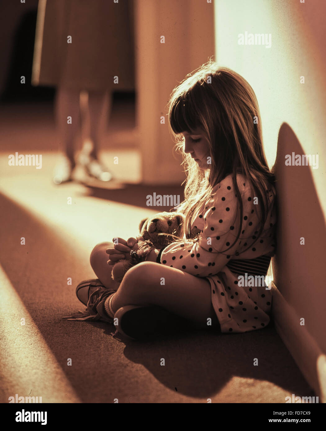 Adolescent sad girl sitting in hallway with stuffed animal Stock Photo