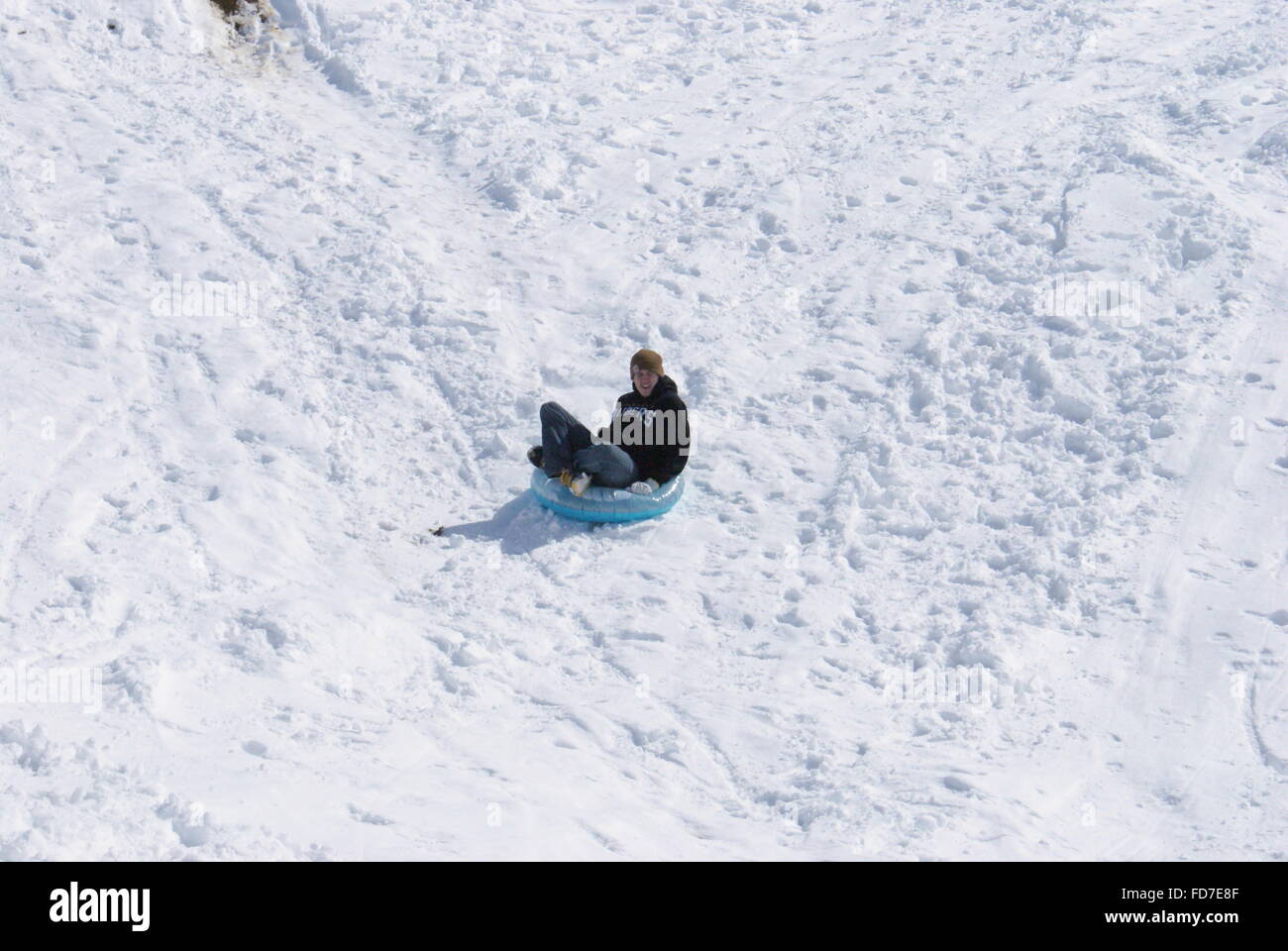 Teenage boy snow tubing down a hill. Stock Photo
