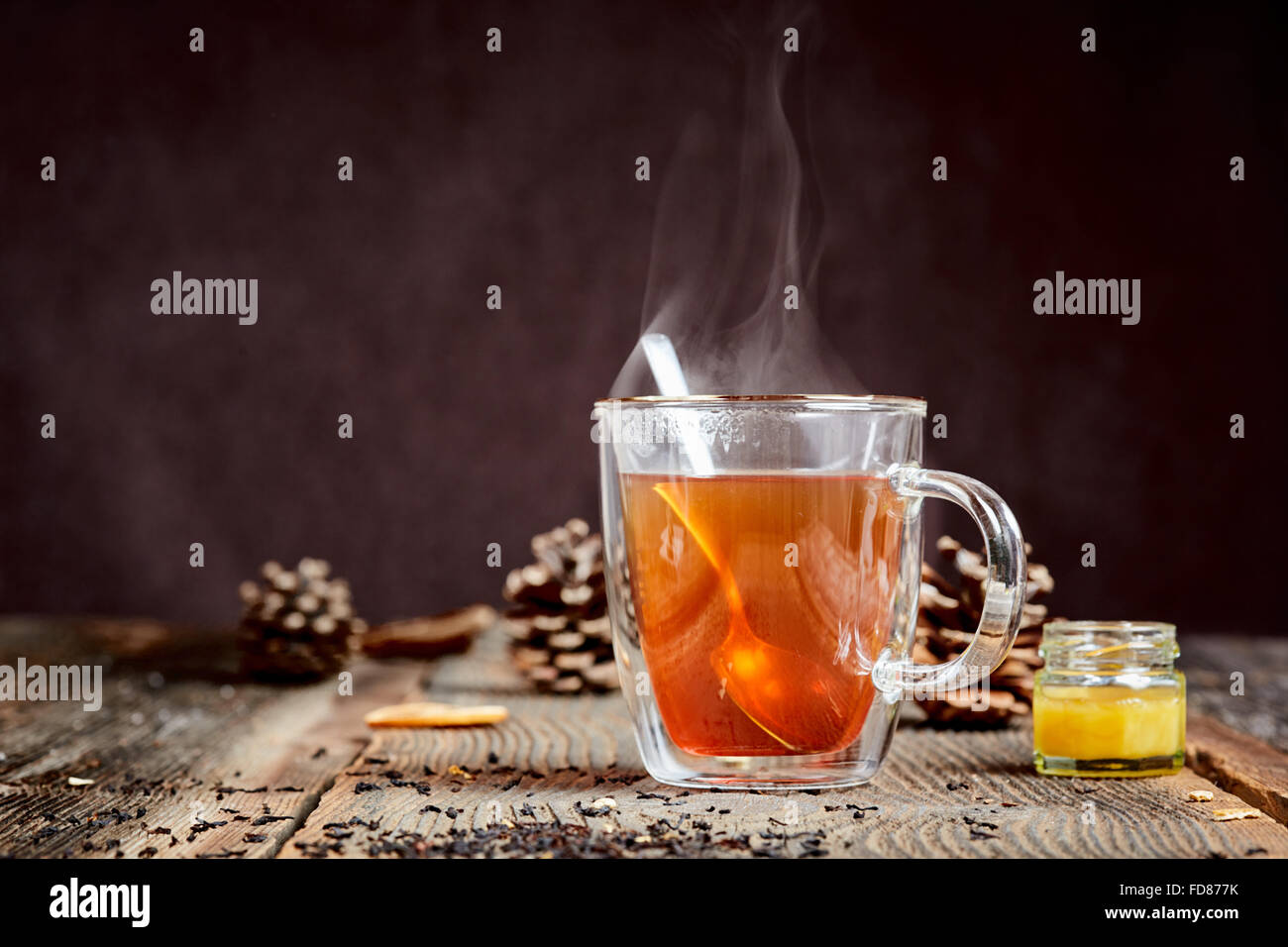 Hot black tea with steam and a little honey pot on a wooden table Stock Photo