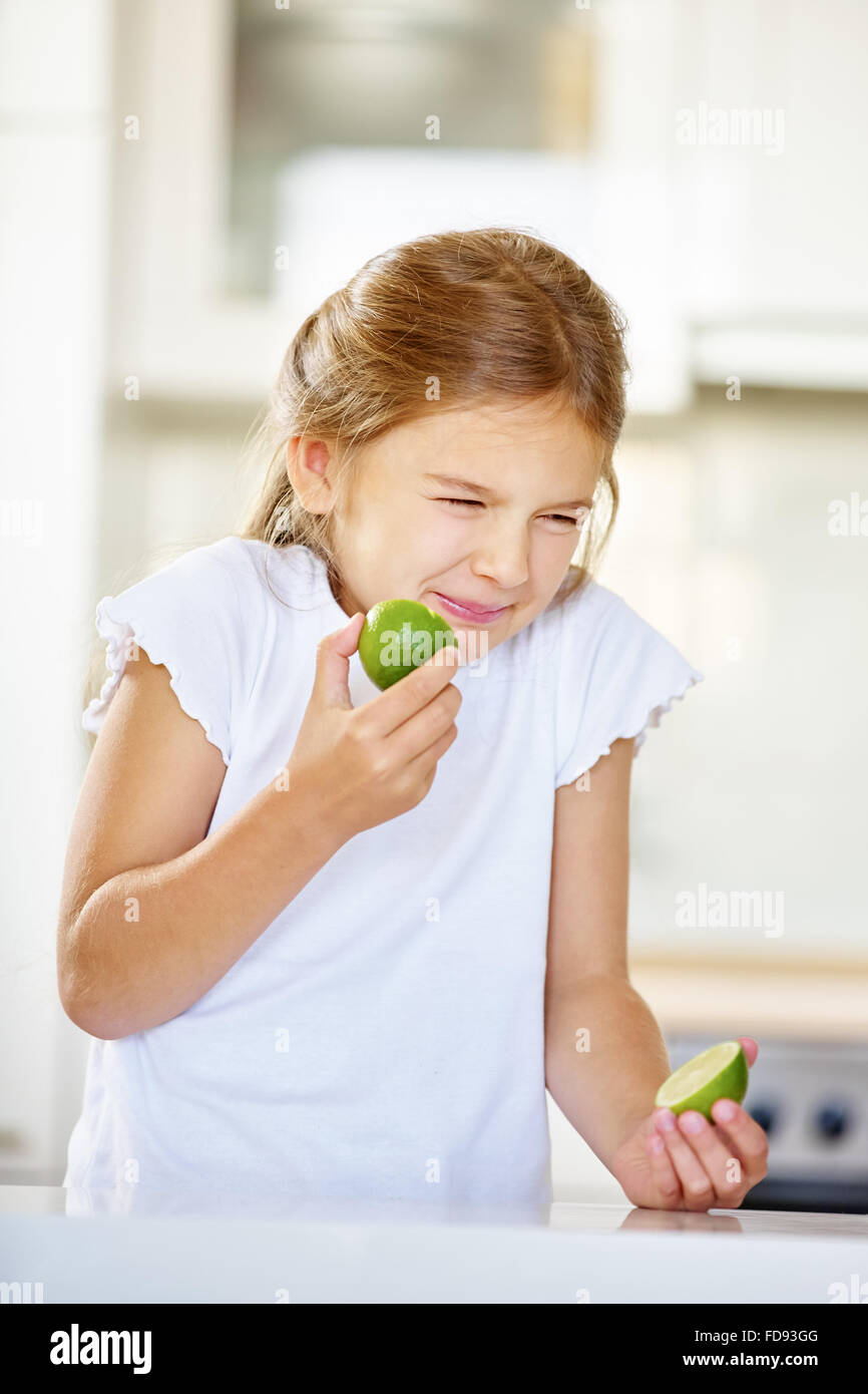 Girl trying to eat lime fruit and making a grimace Stock Photo