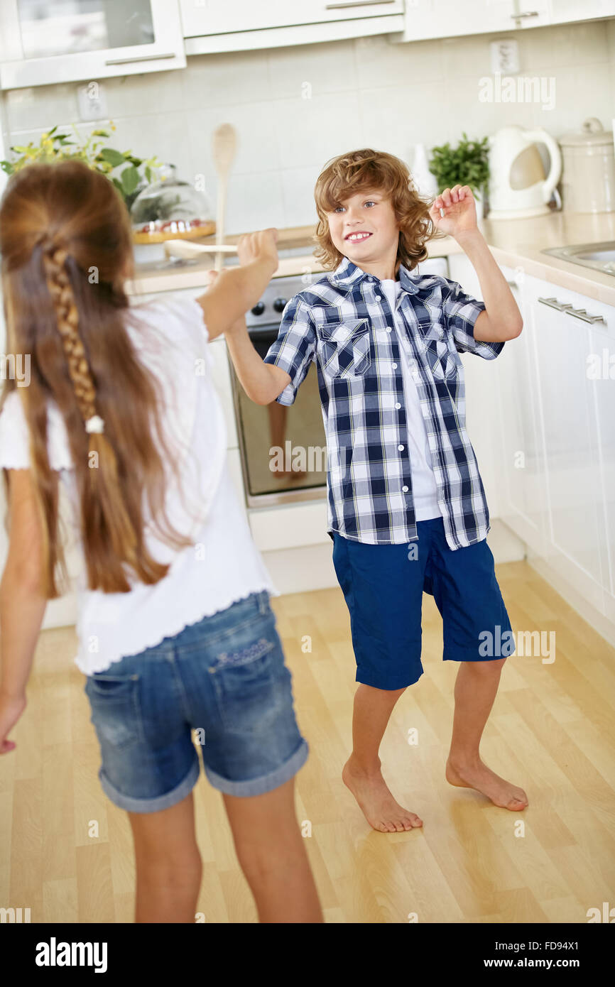 Two kids fighting with wooden spoons in fun in a kitchen Stock Photo