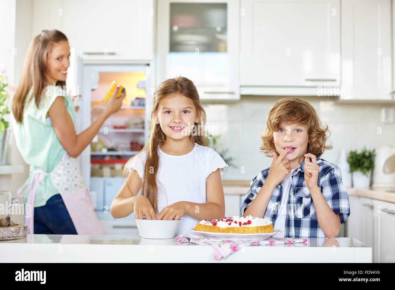 Mother and two children baking and tasting a fruit cake in the kitchen Stock Photo