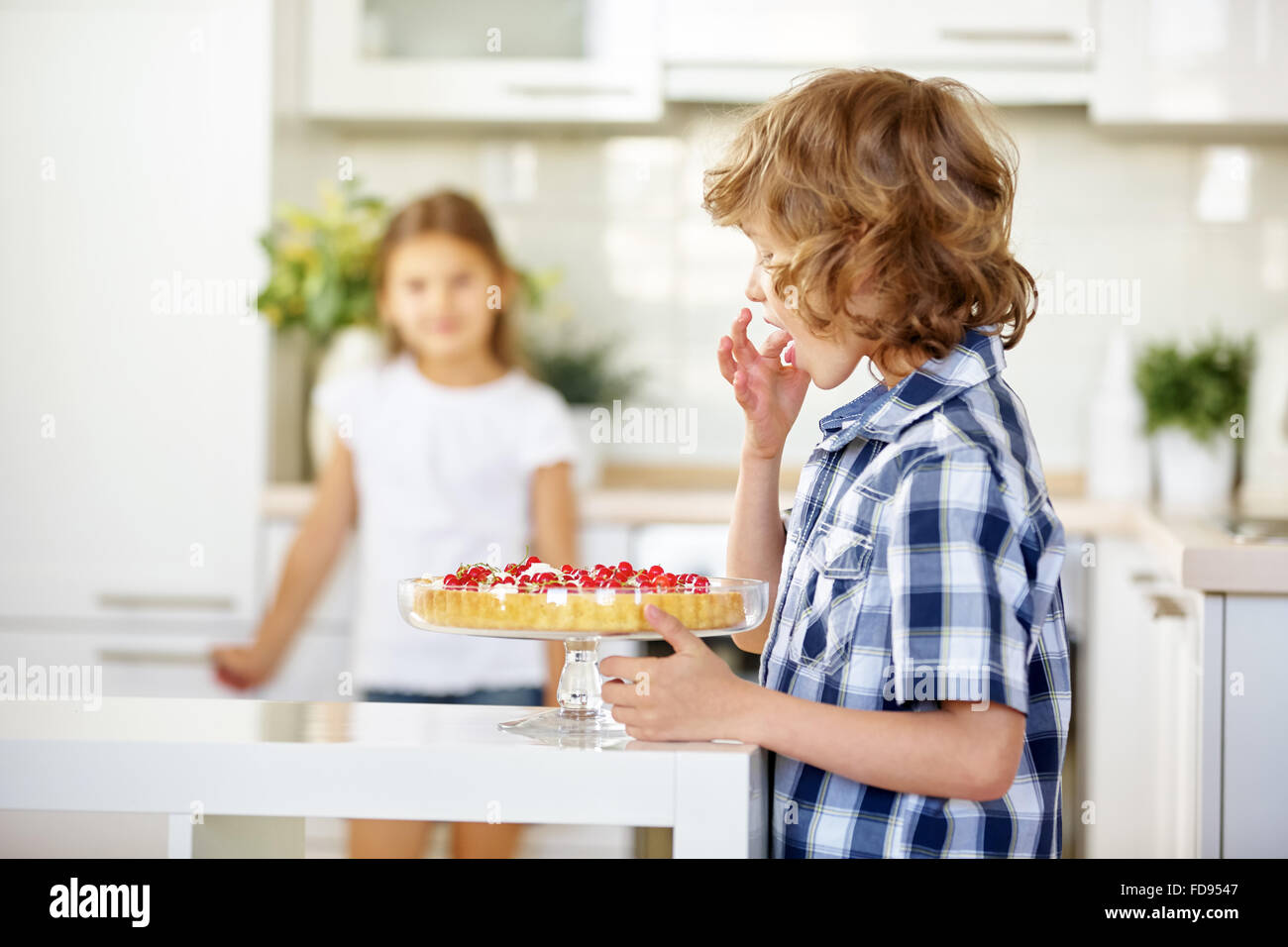 Boy tasting from fresh fruit cake with red currants in the kitchen Stock Photo
