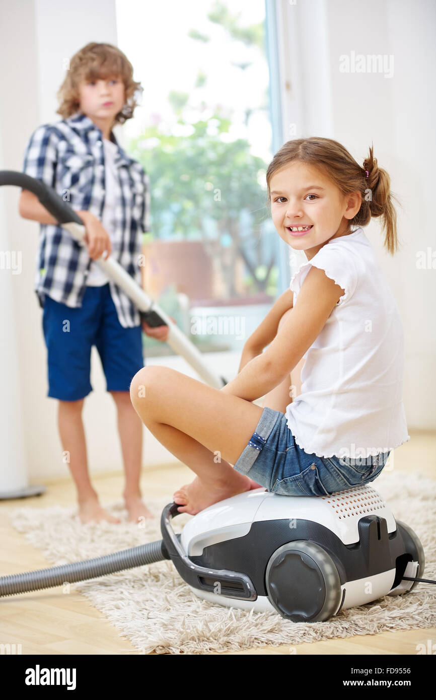 Two happy siblings doing housecleaning with vacuum cleaner Stock Photo