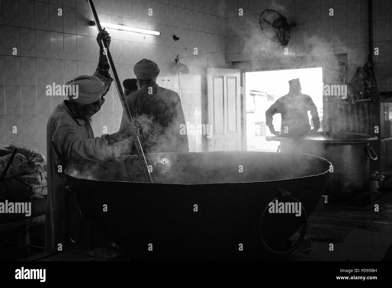 Sikh man stirs large pot of food at volunteer community kitchen, Delhi India Stock Photo