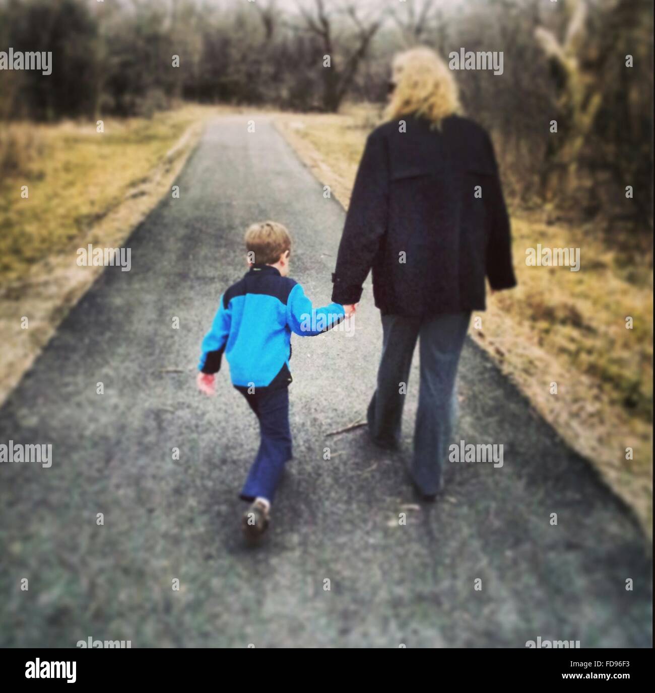 Rear View Of Woman And Boy Walking On Country Road Stock Photo