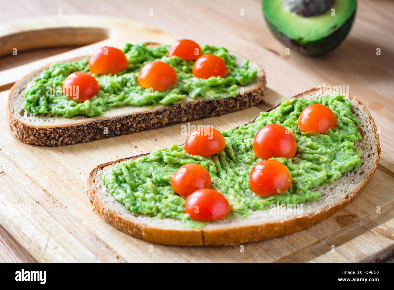 Guacamole and bread. Toast with avocado and cherry tomatoes on wooden cutting board Stock Photo