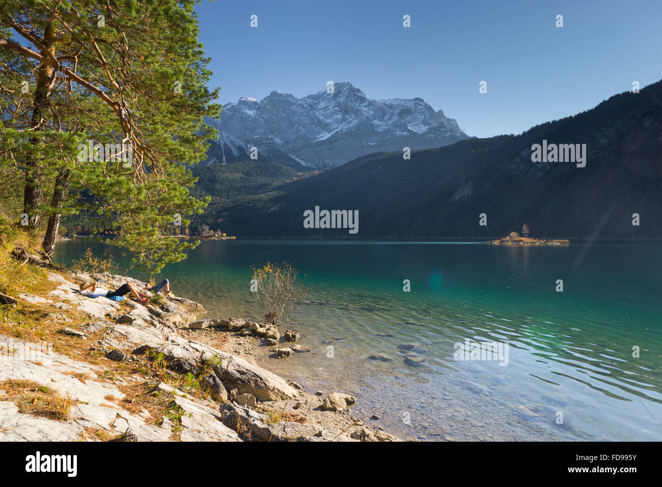 Two women sunbathing at lake Eibsee, snow covered Wetterstein mountains and autumn forests,Garmisch-Partenkirchen, Germany Stock Photo