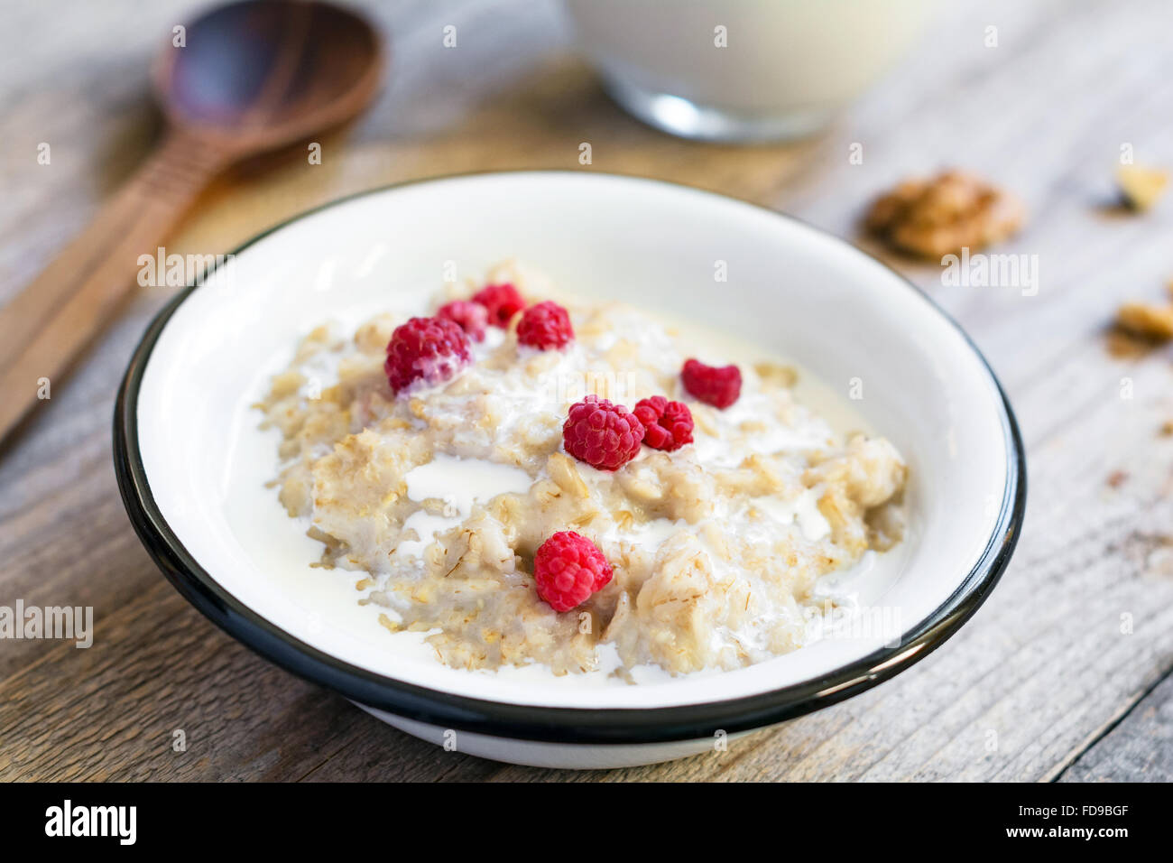 Oatmeal porridge with raspberries and milk on textured wooden table, country style healthy breakfast, Selective focus Stock Photo