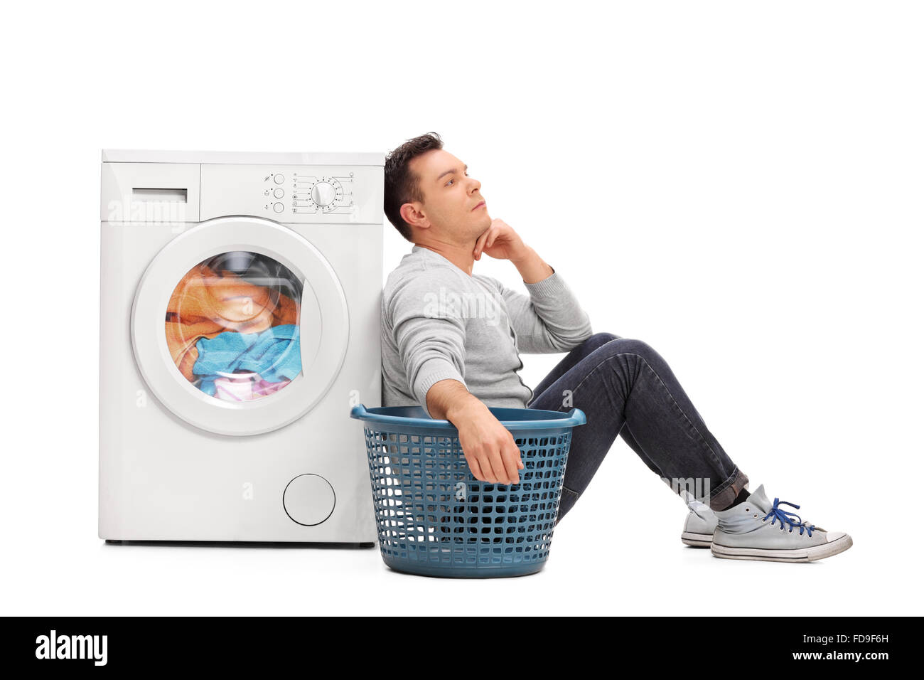 Bored young man sitting by a washing machine and waiting for the laundry isolated on white background Stock Photo
