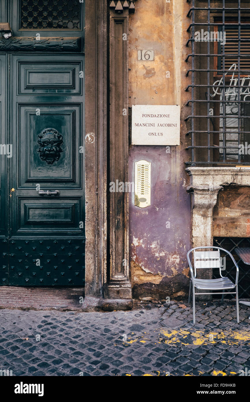 A worn wall and elegant door with a silver chair positioned for people-watching in Rome, Italy Stock Photo