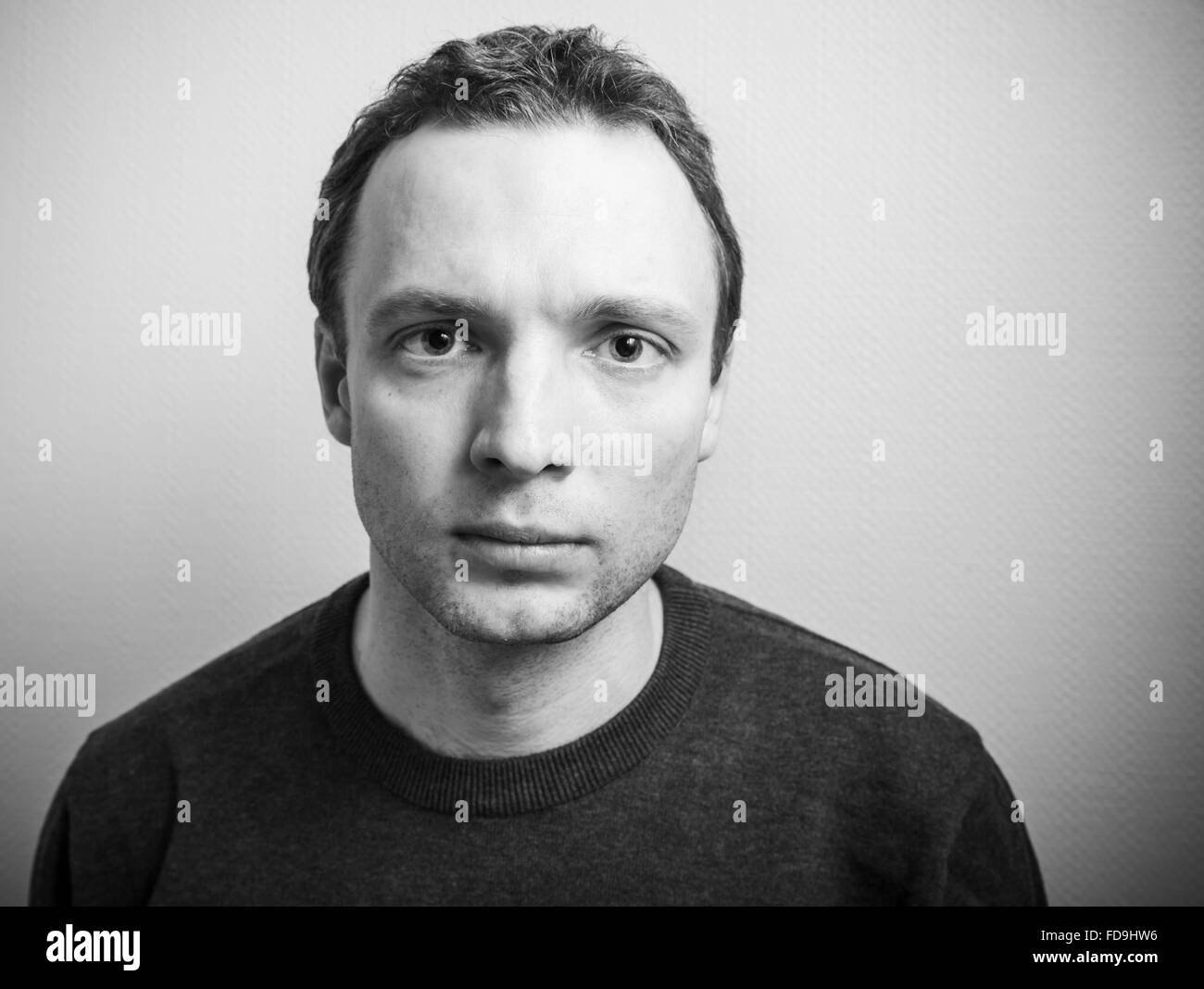 Young serious Caucasian man studio portrait over gray wall background, black and white photo Stock Photo