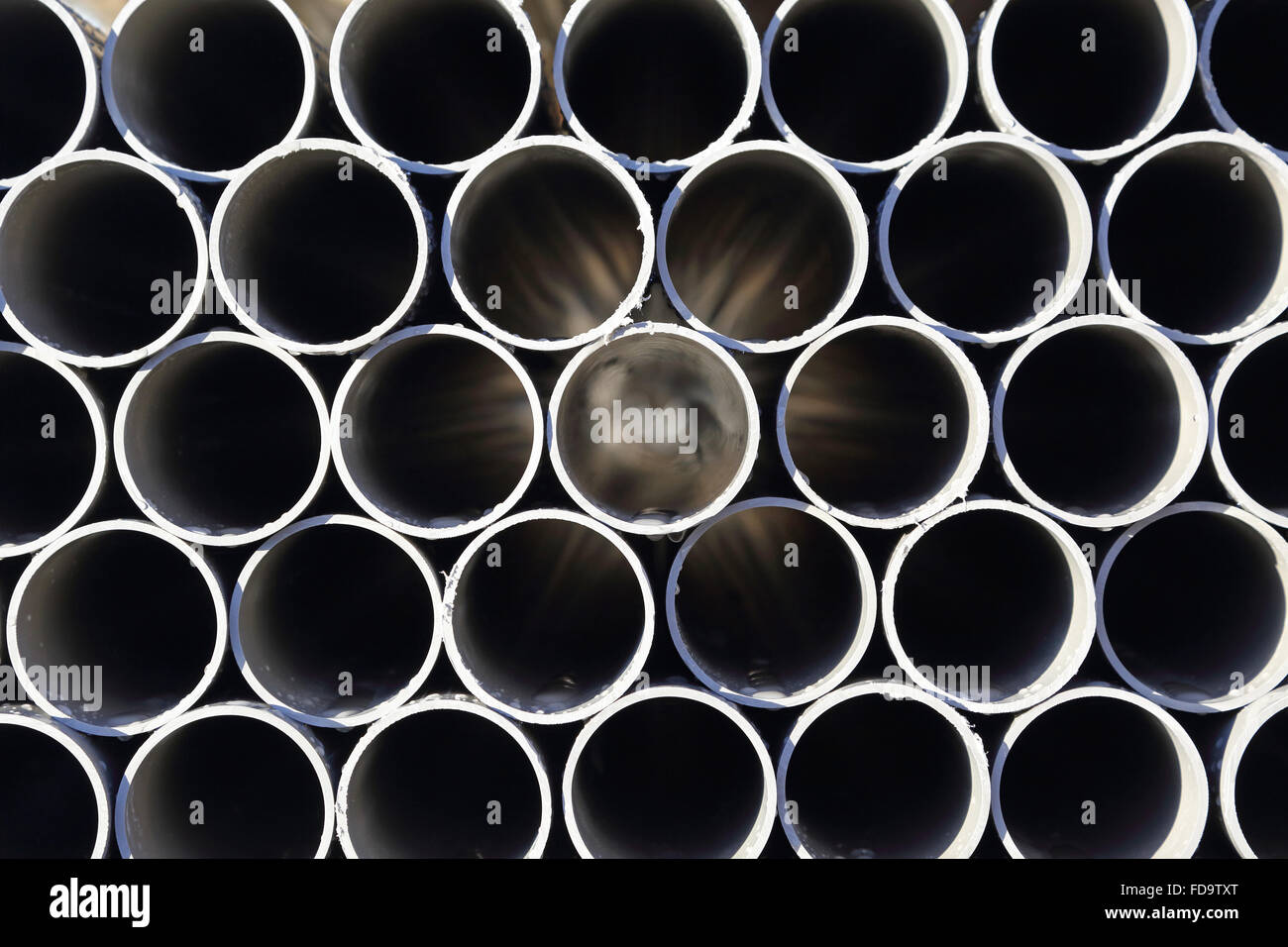 closeup of grey, plastic water pipes stacked in an outdoor yard for
