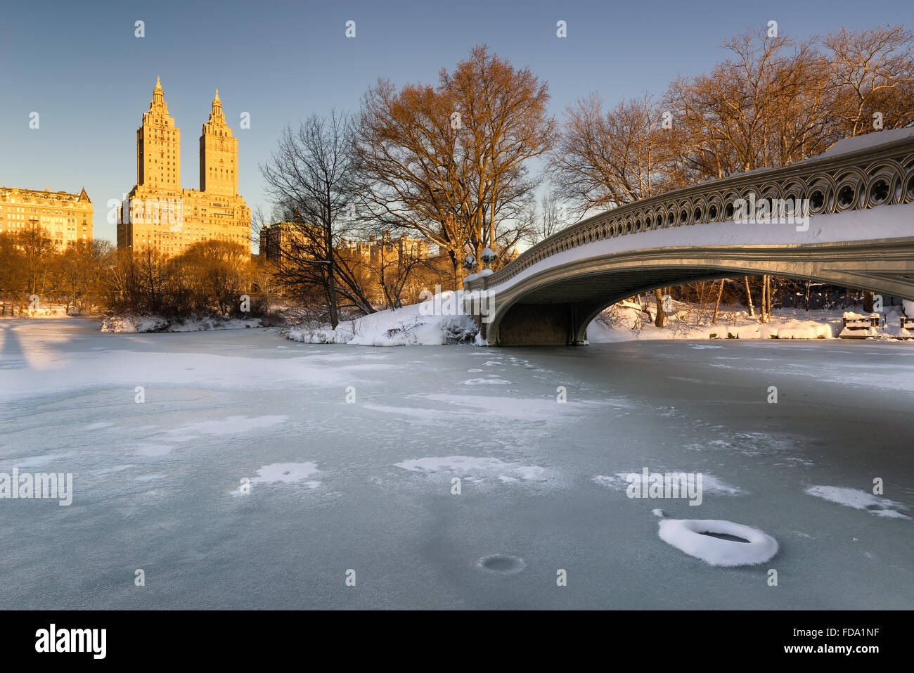 Cold Central Park winter sunrise on the frozen Lake with the Bow Bridge and Upper West Side buildings. Manhattan, New York City Stock Photo