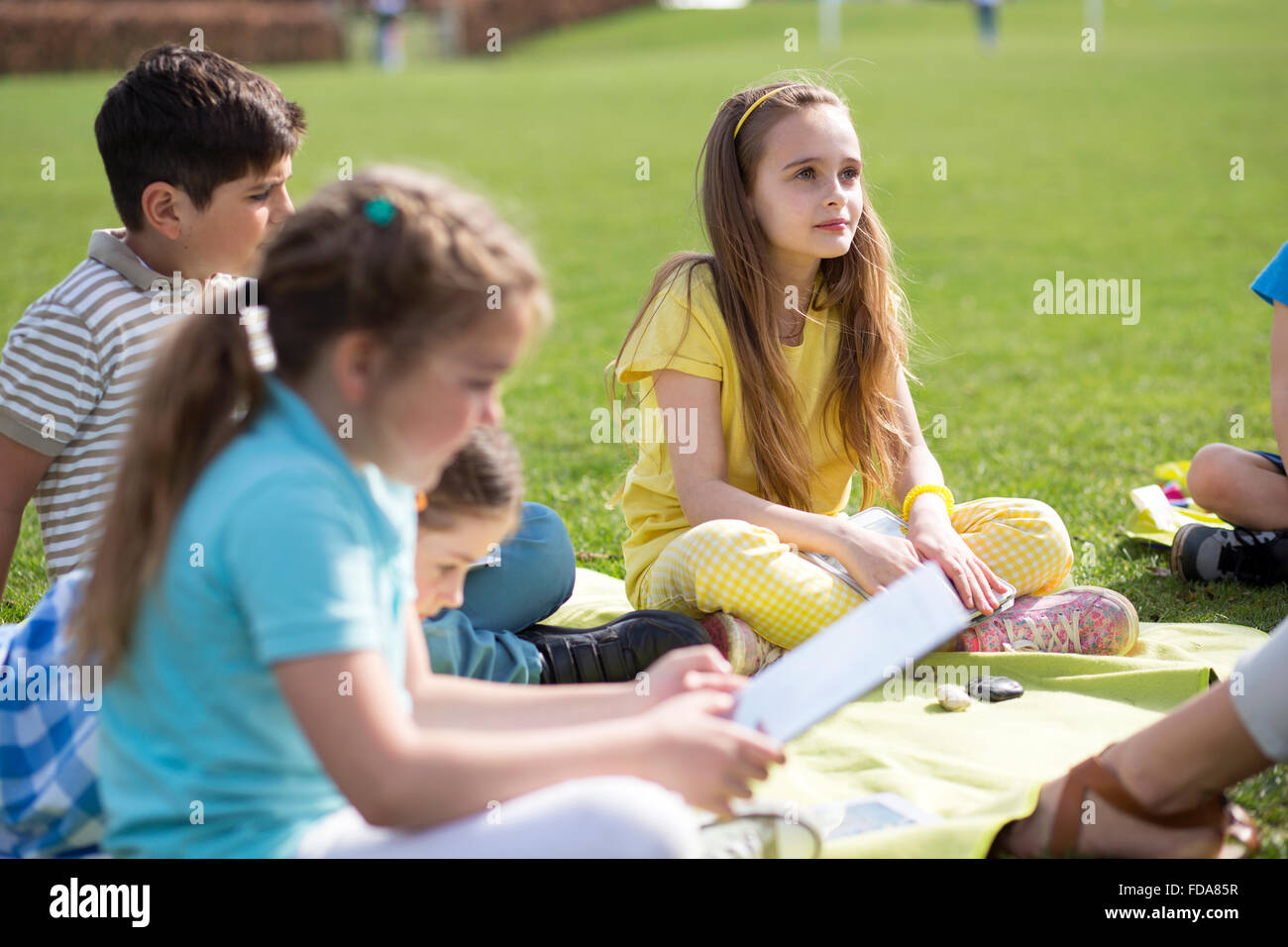 Small group of children sitting on the grass having a lesson outdoors. The children look to be listening and enjoying themself. Stock Photo