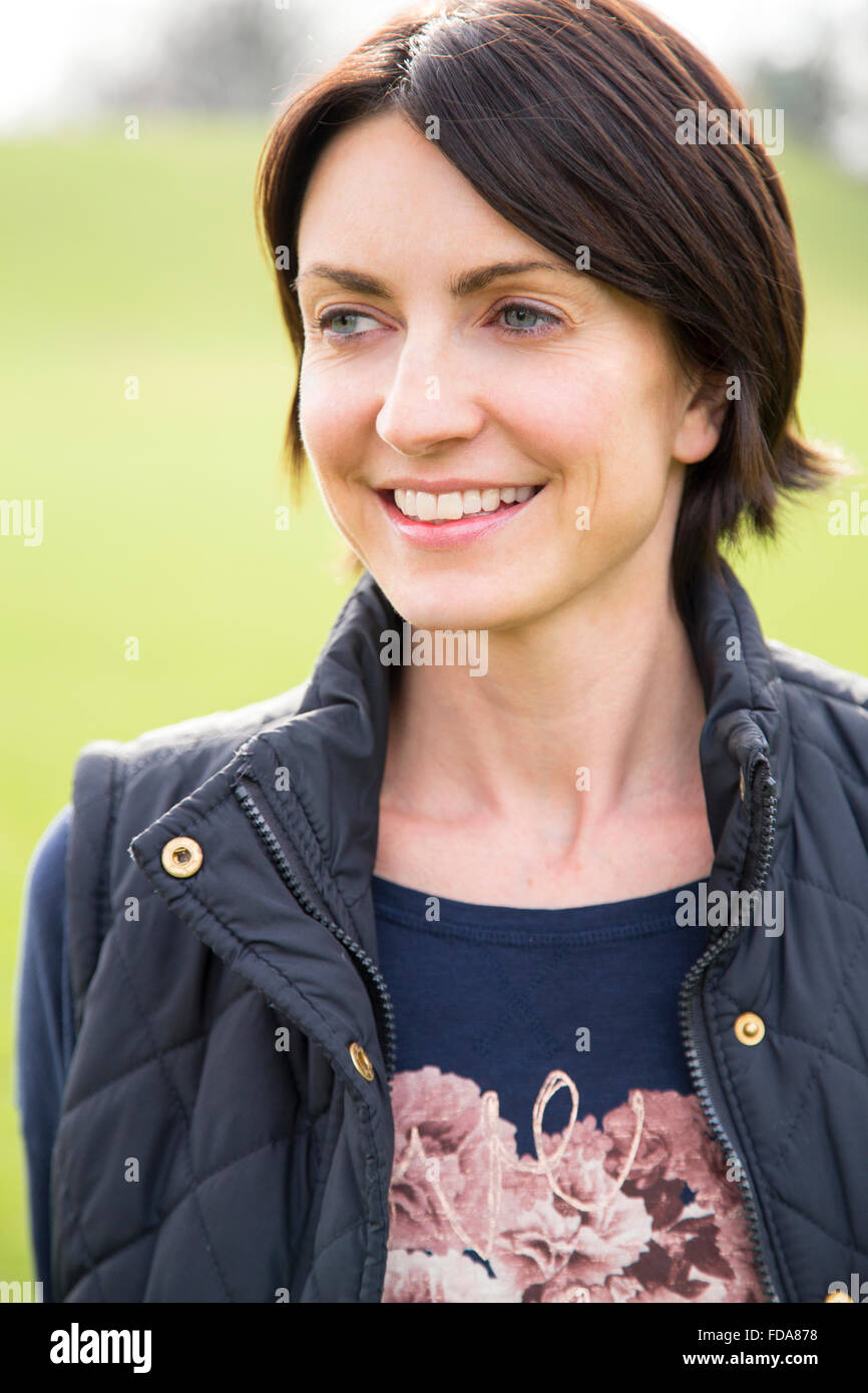 Head and shoulder portrait of a woman looking off into the distance, she is outdoors. A grassy area can be seen behind her, She  Stock Photo
