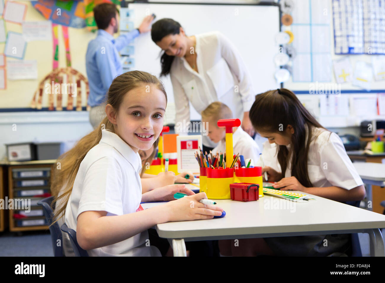 Portrait of a cute young schoolgirl smiling at the camera while sitting ...