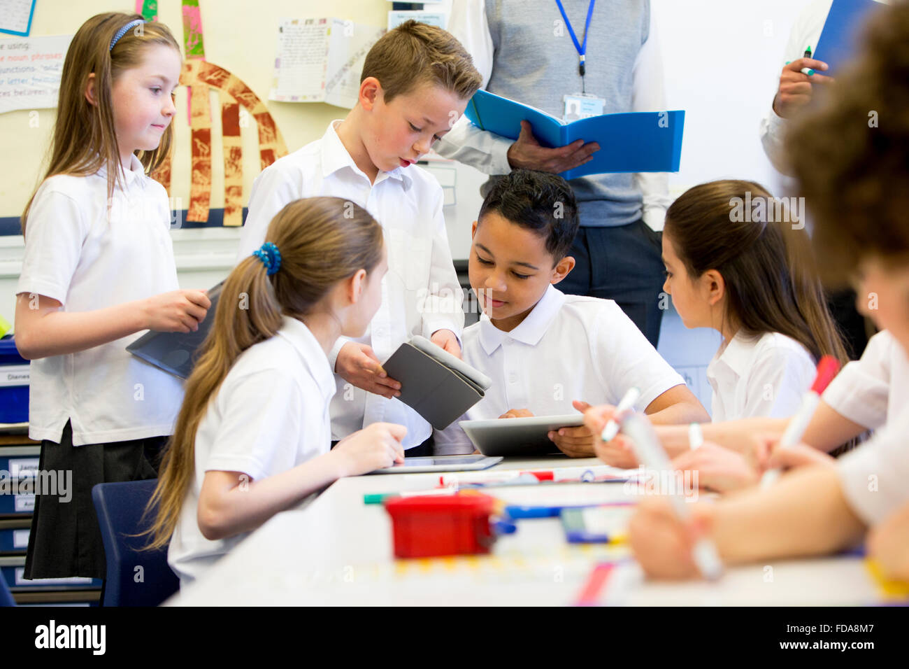 A group of school children can be seen working on digital tablets and ...