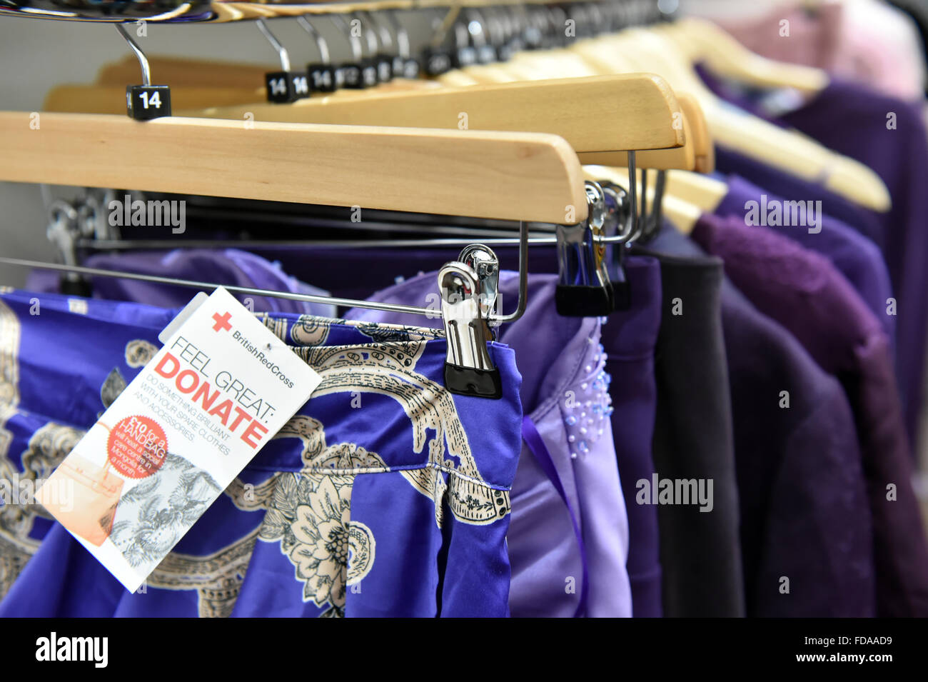 Clothes displayed in a charity shop UK  hanging on coat hangers. Stock Photo
