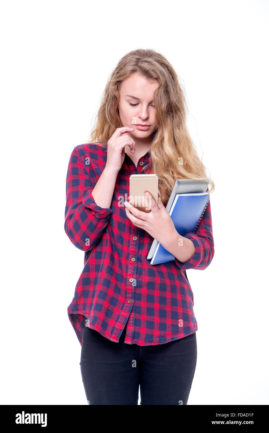Beautiful female student using her phone while carrying her books on a white background. She is wearing casual clothing and is c Stock Photo
