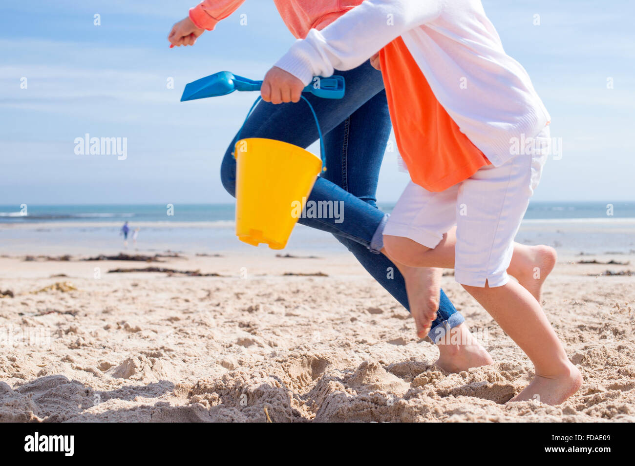 Mother and Daughter running along the beach. Only their legs can be seen, the little girl is holding a bucket and spade. Stock Photo