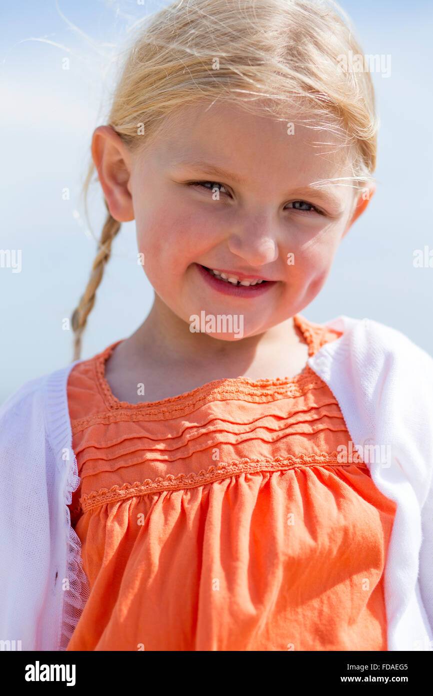 Close up of a beautiful little girl outdoors. She is wearing casual clothing and smiling at the camera. Stock Photo