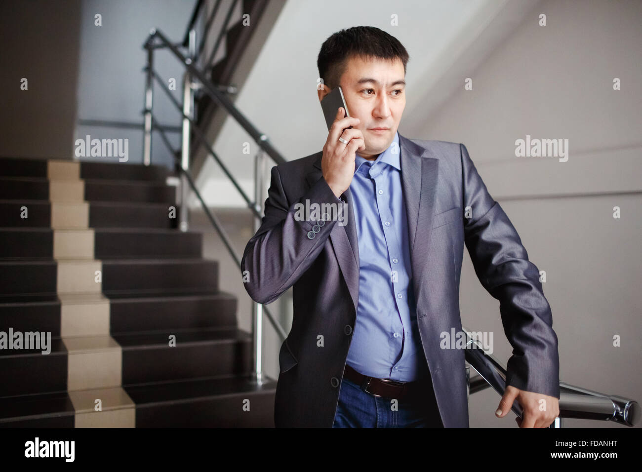 Businessman with phone in his hand makes call while on stairs at office building during break, wearing suit. Business Portrait of a male mid-asian appearance. Stock Photo