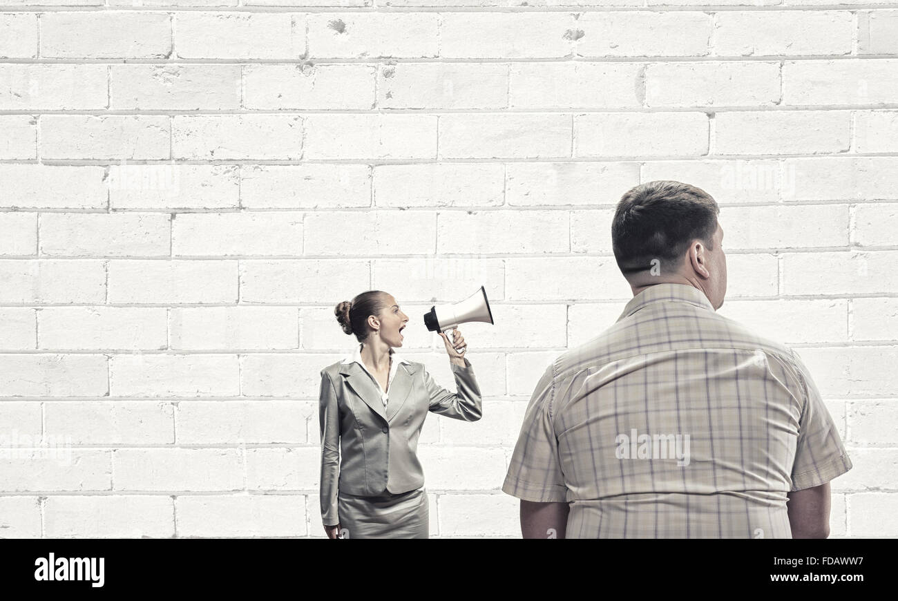 Furious woman screaming agressively in megaphone at man Stock Photo