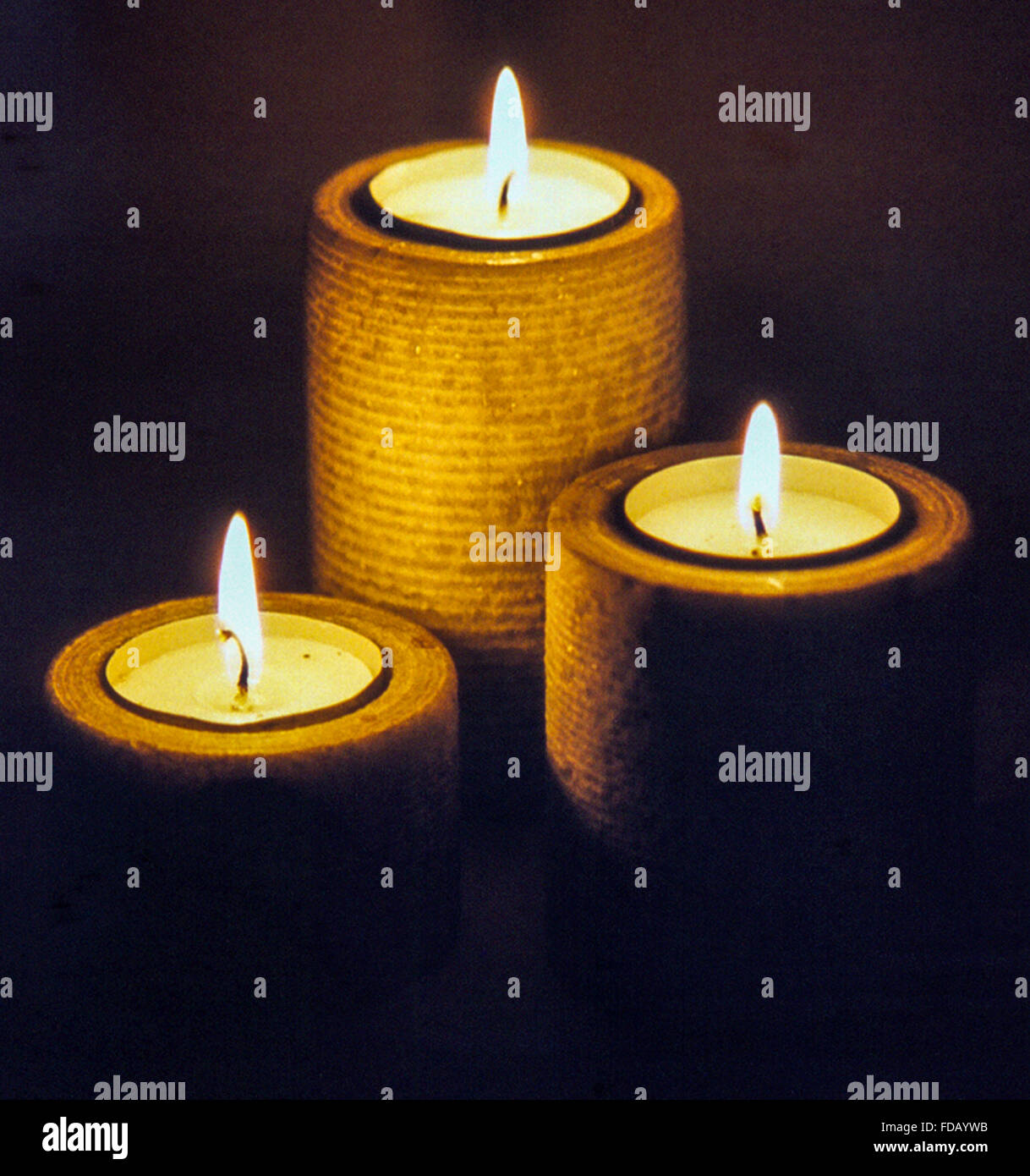 Three lit candles of different heights glowing against a black background Stock Photo